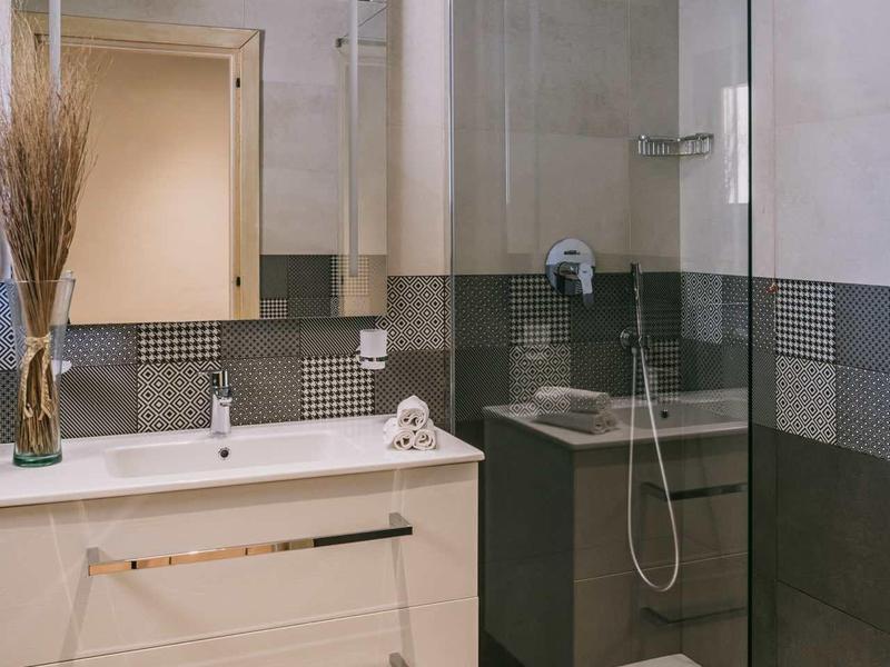 Bagno moderno con lavabo bianco, grande specchio e doccia walk-in in vetro.