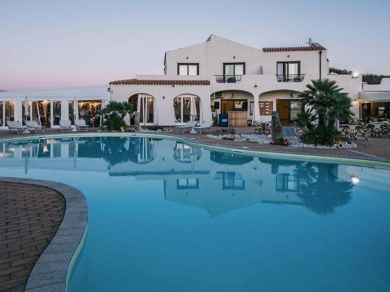 Complesso alberghiero moderno con grande piscina e lettini al tramonto.