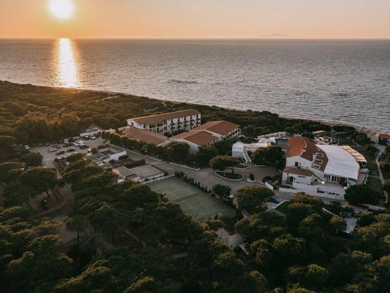 Complesso alberghiero costiero con piscina e vista mare al tramonto.
