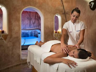 Vrouw krijgt een massage in een sfeervol spa-vertrek met warme, aardse muren en kaarslicht.