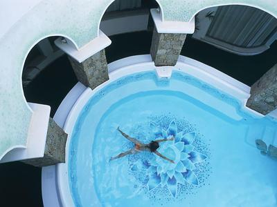 Persoon zwemt in een rond zwembad met bogen en zuilen eromheen.