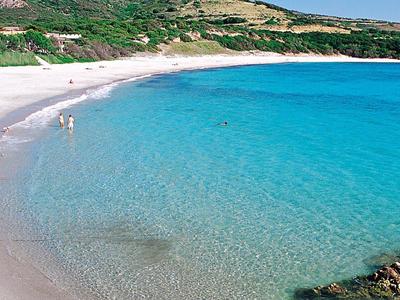 Helder turquoise water bij een gebogen wit zandstrand met groen in de achtergrond.