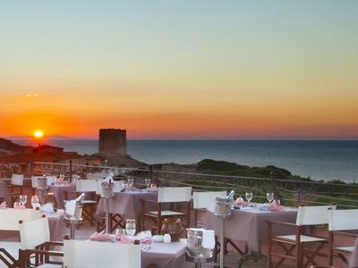 Buitenrestaurant met zitplaatsen bij zonsondergang met oceaan en kust op de achtergrond.