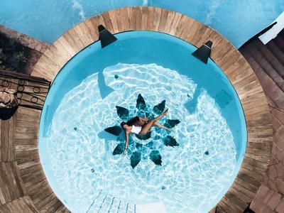 Rond zwembad met stervormig ontwerp, omgeven door houten terras en ligstoelen.