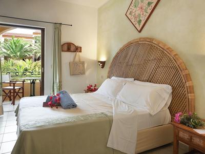 Gezellige hotelkamer met kingsize bed, rotan hoofdeinde en balkon met uitzicht op tropische planten.