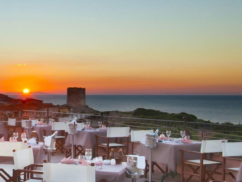 Buitenrestaurant met zitplaatsen bij zonsondergang met oceaan en kust op de achtergrond.