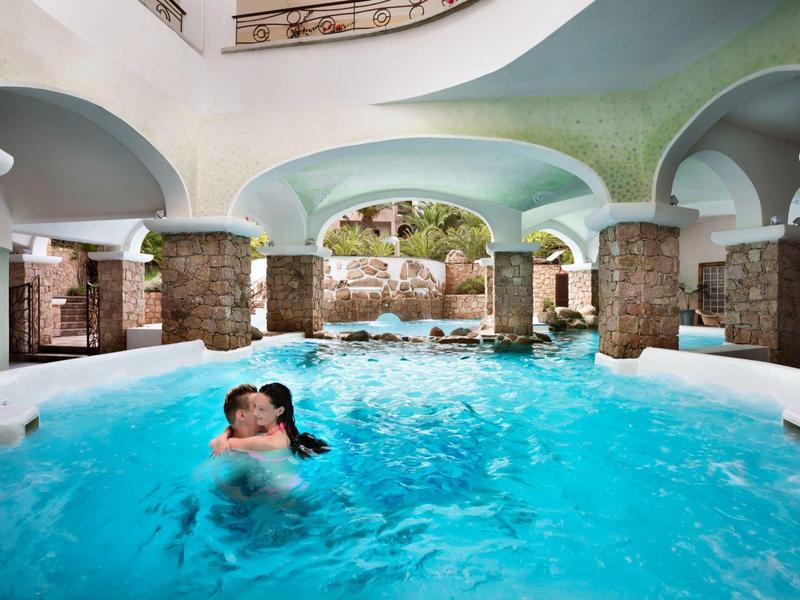 Overdekt hotelzwembad met bogen, stenen pilaren en mensen die van het water genieten.
