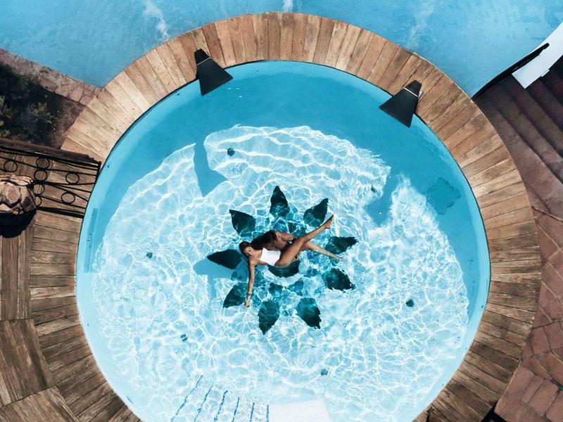 Rond zwembad met stervormig ontwerp, omgeven door houten terras en ligstoelen.