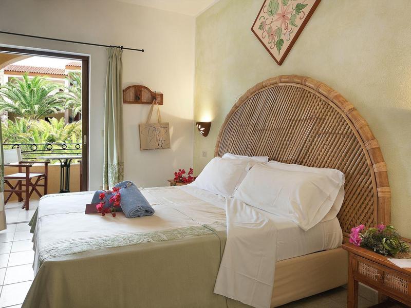 Gezellige hotelkamer met kingsize bed, rotan hoofdeinde en balkon met uitzicht op tropische planten.