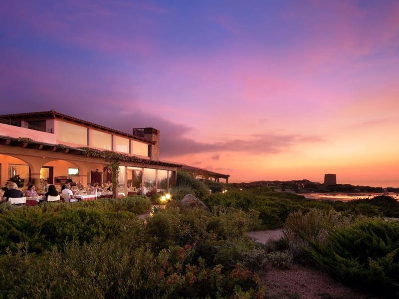 Hotelrestaurant aan zee met buiten dineren bij zonsondergang onder een kleurrijke lucht.