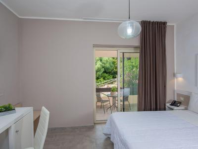 Chambre d'hôtel lumineuse avec lit double, bureau et terrasse donnant sur un jardin.