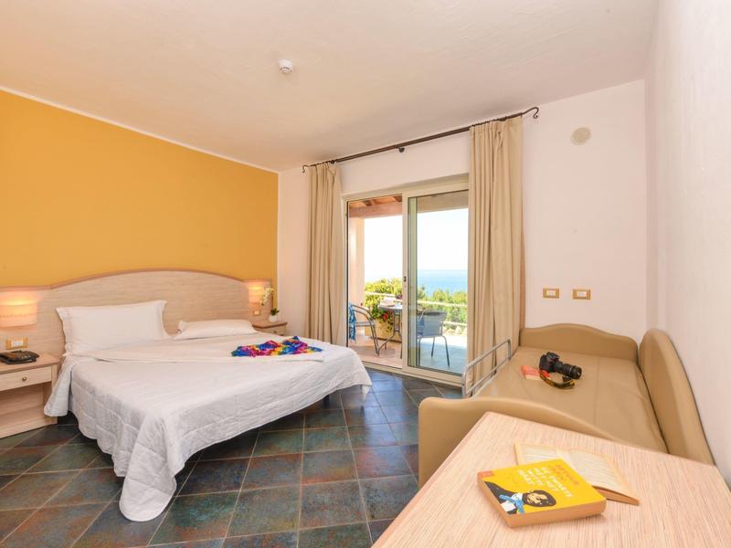 Camera d'hotel luminosa con letto matrimoniale, divano e vista sul balcone con mare