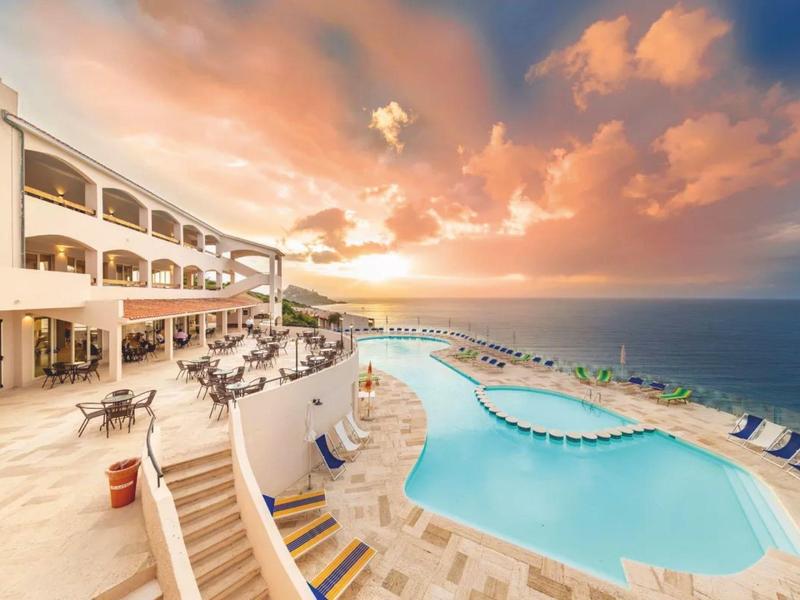 Hotel di lusso con terrazza e piscina con vista sul mare al tramonto.