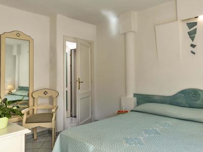 Camera d'hotel luminosa con letto grande, sedia, specchio e pianta.