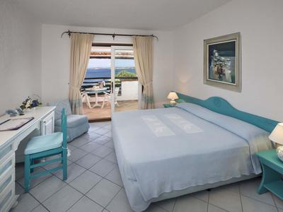 Camera d'hotel luminosa con letto matrimoniale e balcone con vista mare alla luce del giorno.