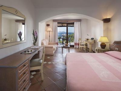 Camera d'hotel luminosa con letto matrimoniale, scrivania, sedie e vista su balcone e mare.