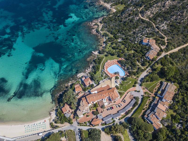 Veduta aerea di un resort costiero con spiagge, acque limpide e diversi edifici.