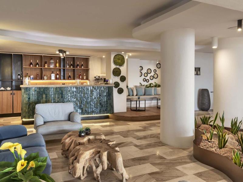 Hall d'hotel moderno con area salotto, bancone e piante decorative.