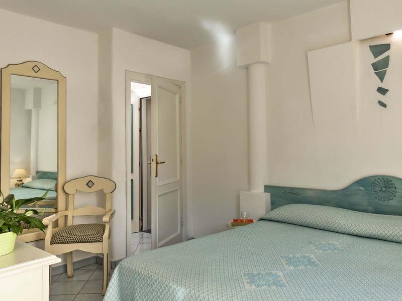 Camera d'hotel luminosa con letto grande, sedia, specchio e pianta.