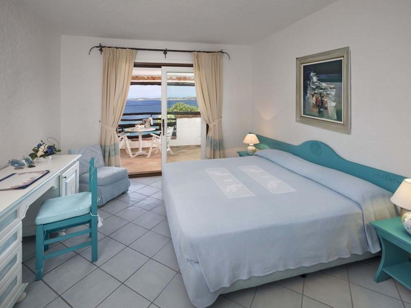 Camera d'hotel luminosa con letto matrimoniale e balcone con vista mare alla luce del giorno.