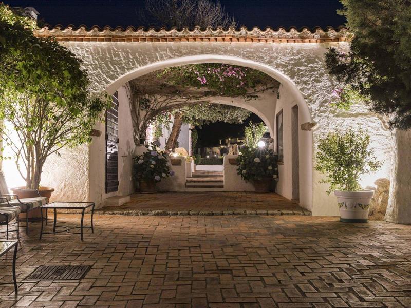 Passaggio ad arco illuminato con piante in un cortile tranquillo di un hotel di notte.