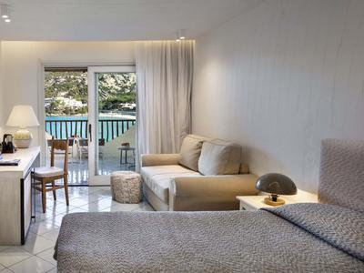 Moderní hotelový pokoj s manželskou postelí, pohovkou a balkonem s výhledem do přírody.