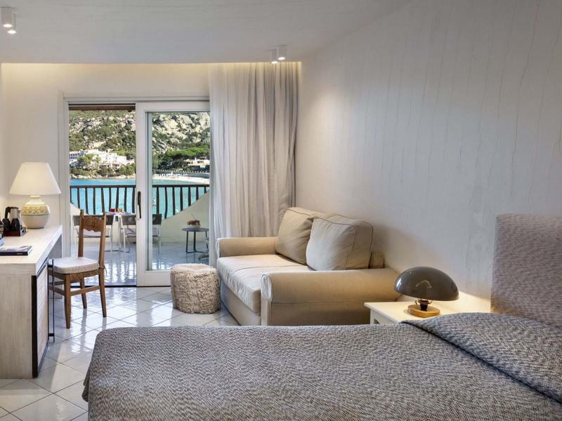 Moderní hotelový pokoj s manželskou postelí, pohovkou a balkonem s výhledem do přírody.