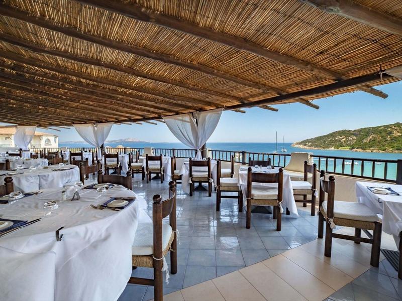 Otevřená restaurace s dřevěnou střechou a výhledem na moře, stoly s bílými prostírkami.