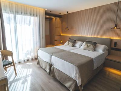 Habitación de hotel moderna con dos camas individuales, detalles en madera y luz natural junto a la ventana.