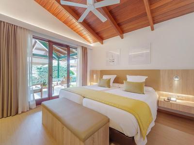 Habitación de hotel luminosa con cama doble, techo de vigas de madera y acceso a terraza con plantas.