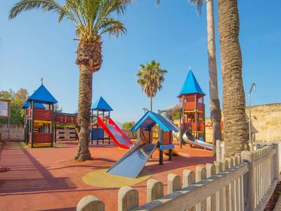 Área de juegos infantiles con estructuras coloridas y palmeras bajo cielo despejado.