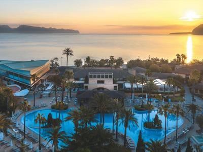 Amanecer sobre una piscina de hotel con palmeras en la costa y montañas al fondo.
