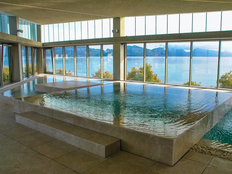 Piscina interior con grandes ventanas que ofrecen vistas al lago y al paisaje montañoso.
