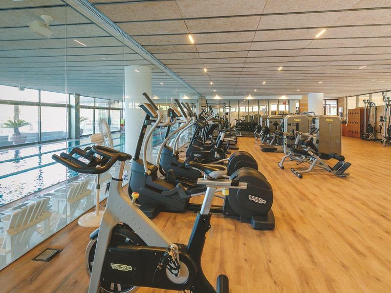 Sala de fitness luminosa con equipos modernos y suelo de madera en un hotel.