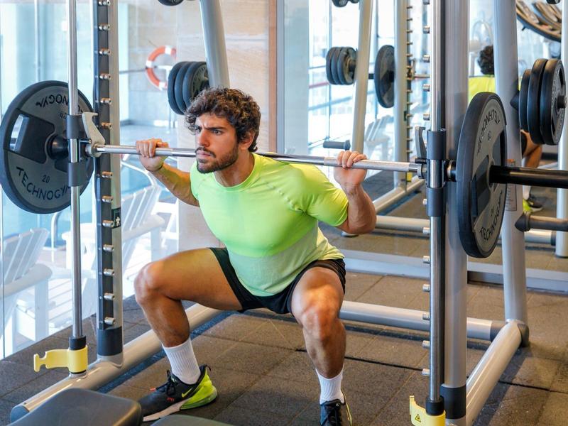 Hombre haciendo sentadillas en el gimnasio del hotel con pesas en la barra.
