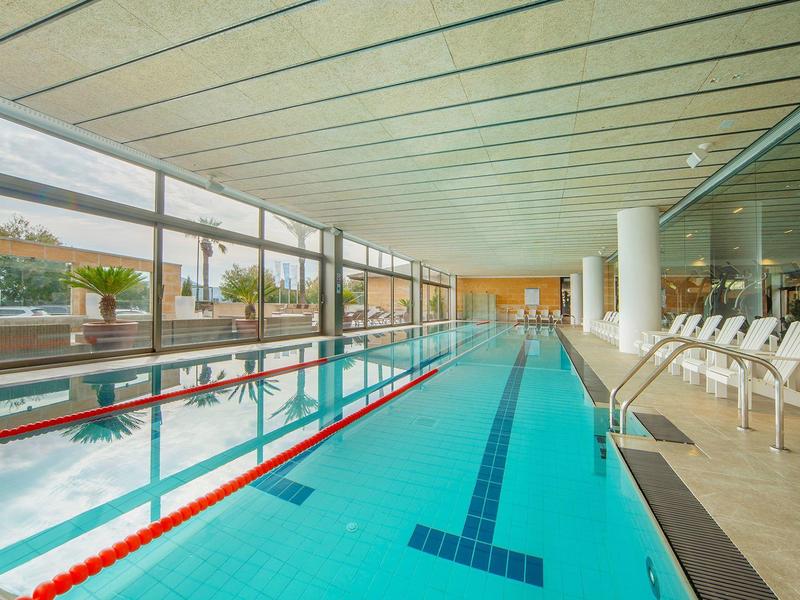 Piscina interior estrecha y larga con sillas blancas al lado y ventanas grandes que ofrecen luz natural.