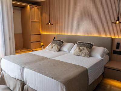 Habitación de hotel moderna con cama doble grande, iluminación suave y tonos neutros.