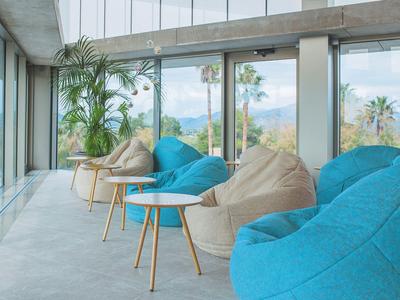 Helle Lounge mit großen Fenstern, blauen und beigen Sitzsäcken und kleinen Holztischen.