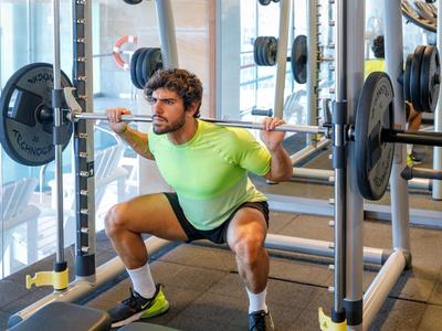 Mann in Sportkleidung macht Kniebeugen mit Langhantel im Fitnessstudio.