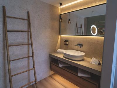 Moderne badkamer met houten ladder, ronde wastafel, grote spiegel en warme verlichting.