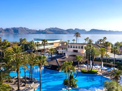 Resort hôtelier de luxe avec grandes piscines, palmiers et vue sur la mer et les montagnes.