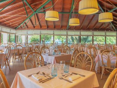 Ruim restaurant met houten meubels en grote ramen met uitzicht op groen.