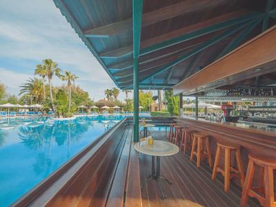 Lichte hotelkamer met twee losse bedden, houten wand, hanglampen en doorzichtige gordijnen.