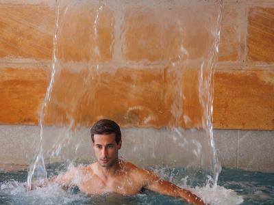 Man zit in een zwembad met water dat achter hem als een waterval valt.