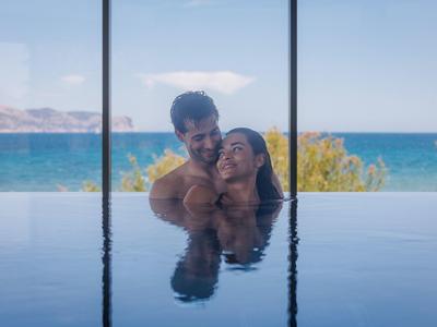 Koppel geniet van een infinity pool met uitzicht op zee en eilanden op een zonnige dag.