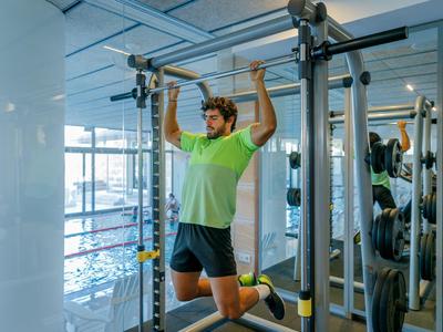 Mann trainiert mit einem Suspension-Trainer in einem modernen Fitnessstudio mit viel Tageslicht.