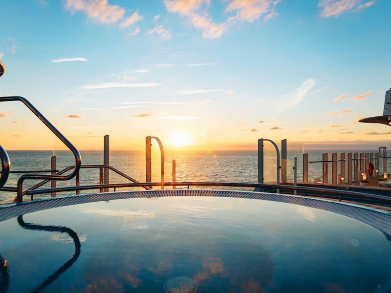 Zonsondergang boven de oceaan vanaf een hotelzwembadterras met leuningen en kalm water.