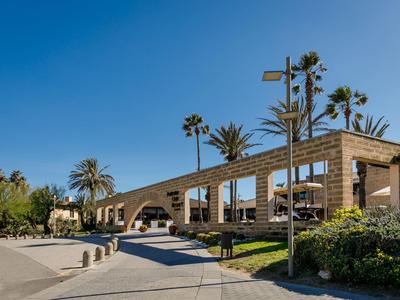 Complexe de bâtiments modernes avec arcades, palmiers et ciel bleu par une journée ensoleillée.