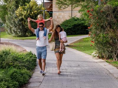 Famille avec un enfant porté sur les épaules marchant sur un trottoir dans un quartier verdoyant.
