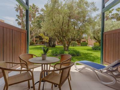Terrasse avec table, chaises et chaise longue offrant une vue sur un jardin verdoyant.